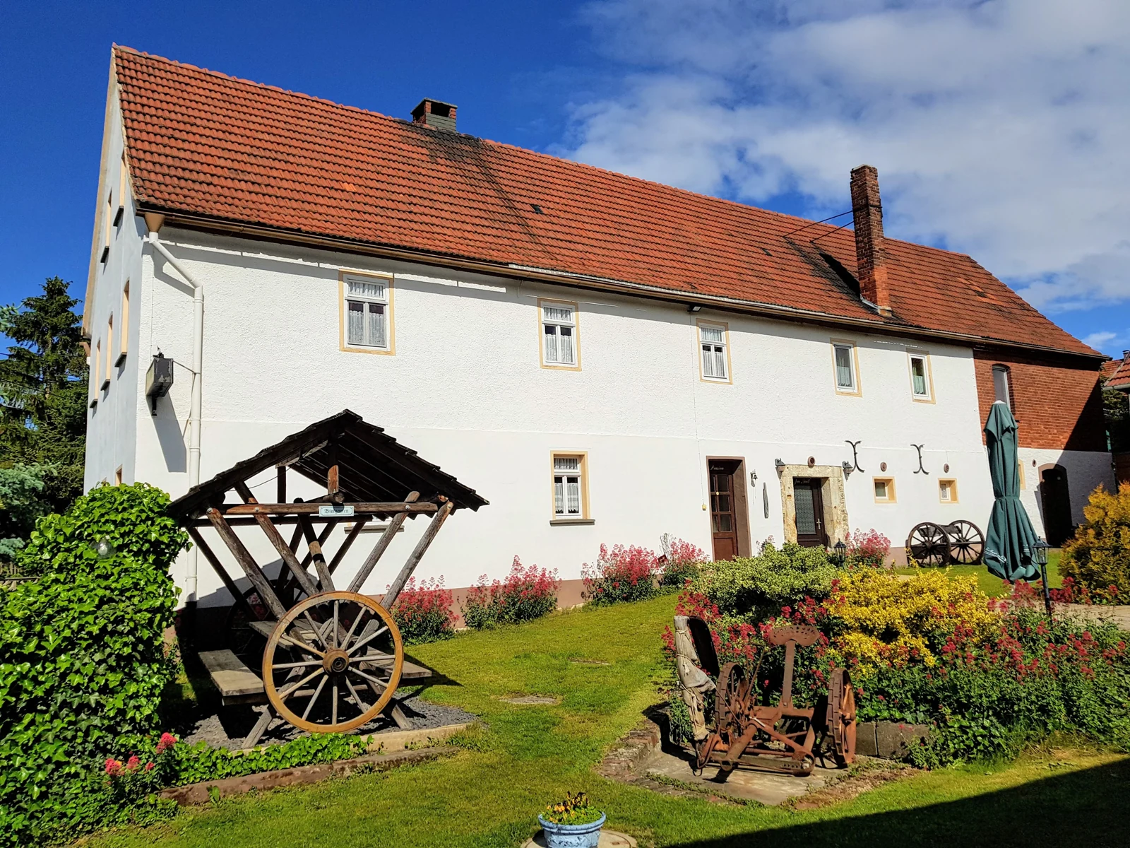 Pension Seisla with white house facade, red brick roof and flowering garden.