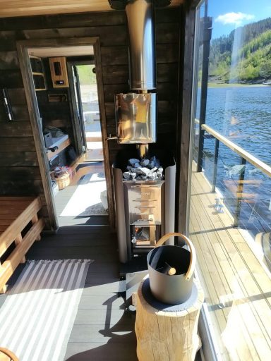 Ein Innenraum mit Holzofen, Eimer und Blick auf das Wasser und die Landschaft.