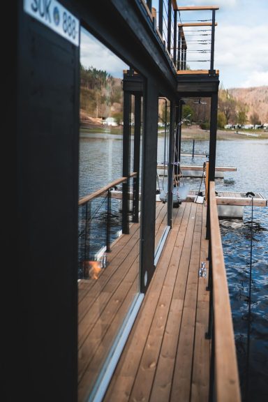 Holzsteg entlang eines Gewässers mit modernen Gebäuden und Blick auf die Landschaft.