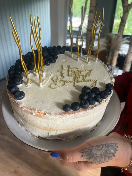 Torte Cremetorte mit Heidelbeeren und goldenen Kerzen auf einem Tisch serviert.
