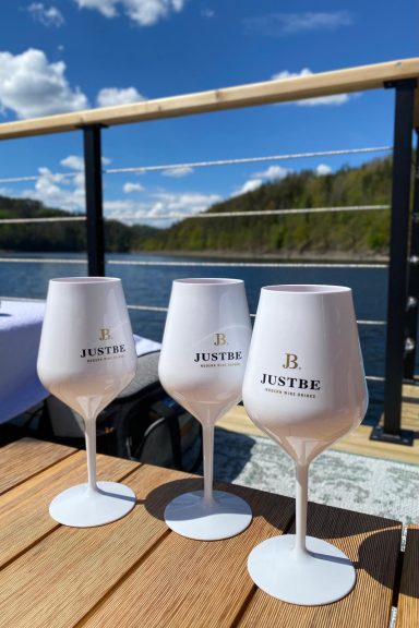 Drei elegante Weingläser auf einem Tisch mit Blick auf das Wasser und bewaldete Berge.