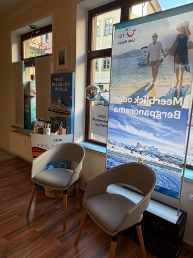 Zwei Stühle neben einem Werbebanner in einem hellen Raum mit großen Fenstern.