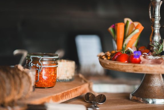 Ein Tisch gedeckt mit Gemüse, einer Marmelade und einem Holzbrett mit Käse.