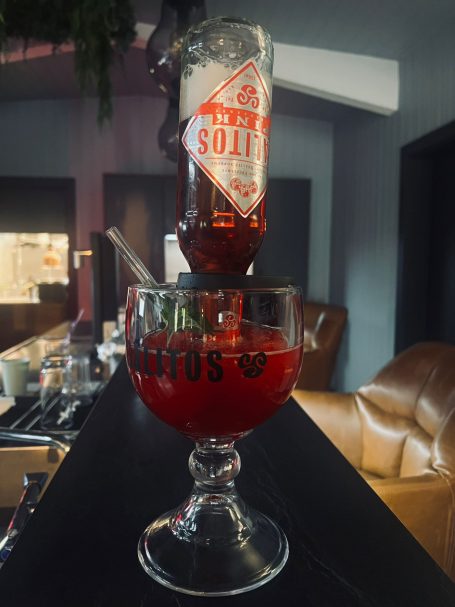 Ein Glas mit einem Drink, darüber eine Flasche rote Spirituose.