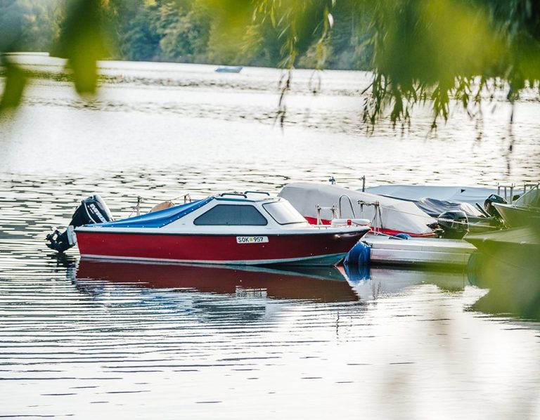 Ein rotes Boot liegt ruhig am Ufer eines glitzernden Gewässer.