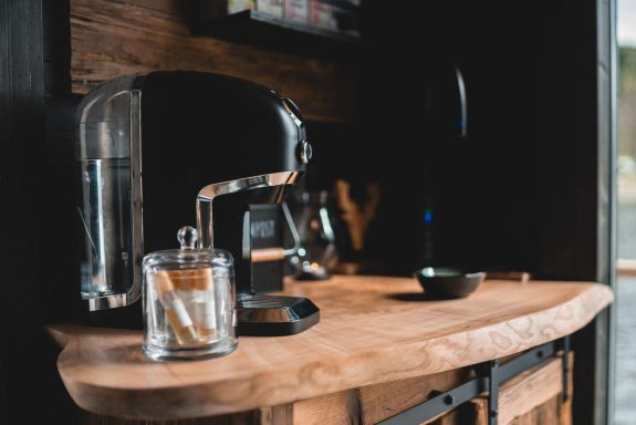 Moderne Kaffeemaschine auf einer Holzarbeitsplatte, daneben Gläser und eine Schale.