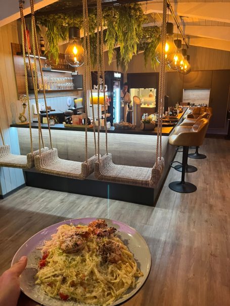 Ein Teller Spaghetti vor einem gemütlichen Restaurant mit Holzinterieur und Bar.