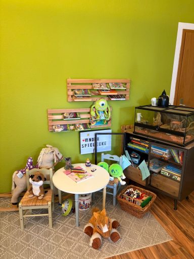 Spielbereich mit Tisch, Stühlen, Spielzeug und einer Tierterrarium an der Wand.