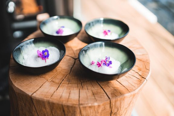 Vier Schalen mit grünem Dessert, garniert mit essbaren Blüten, auf einem Holzstamm.