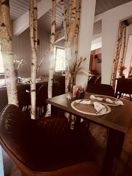 Gemütliches Restaurant mit Holztischen und Birkenstämmen als Dekoration.