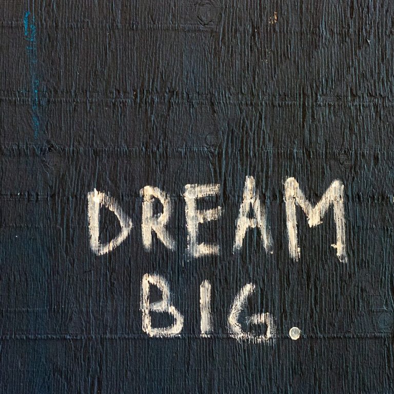 Graffiti mit der Aufschrift "DREAM BIG." auf schwarzem Hintergrund.
