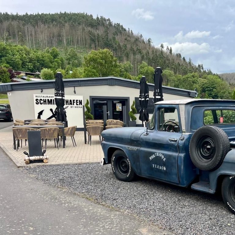 Landidyllisches Café mit einem blauen Oldtimer-Pickup und Terrassenplätzen.